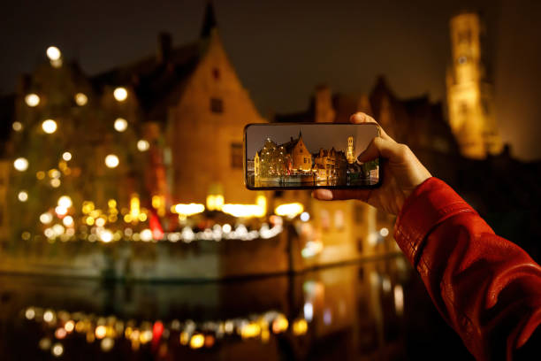 tomando una foto del casco antiguo de bélgica brujas iluminado por la noche. turista con smartphone. - belfort fotografías e imágenes de stock