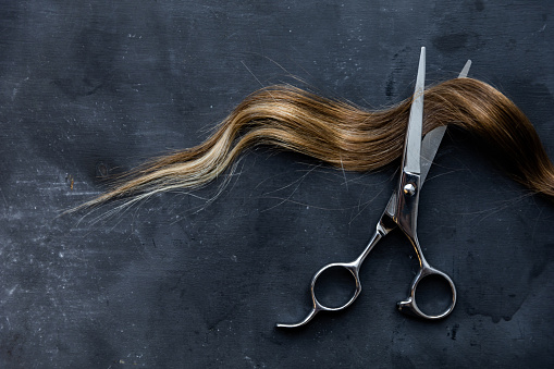 scissors with a lock of hair on a gray textured background, hair cutting, space for text. High quality photo