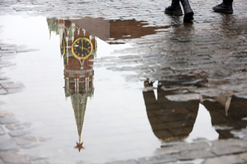 Reflection of Kremlin tower and walking people in a puddle of water, melting snow