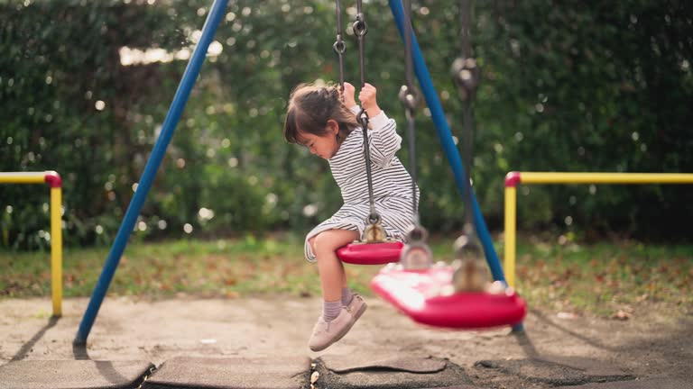 Small girl sitting on swing alone in public park