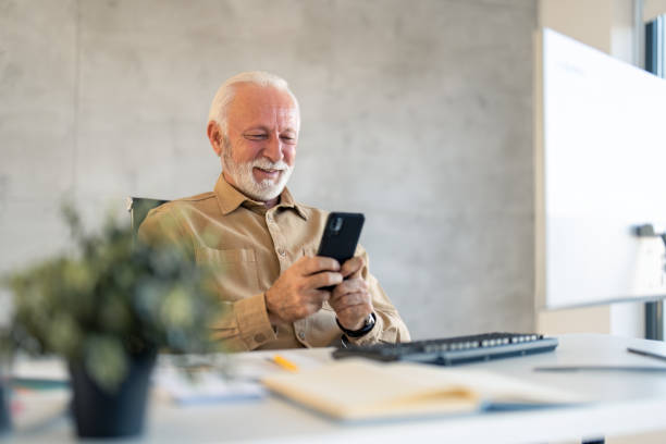 istock Older senior professional employee using cell phone at work in office 1458289732