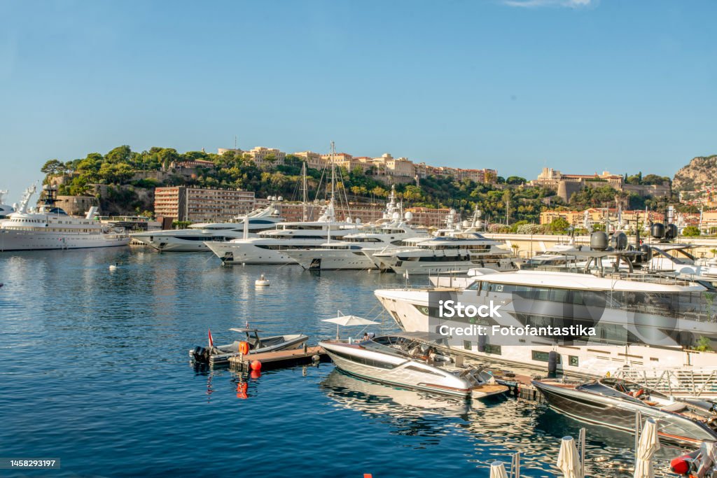 Idyllic view of the harbor (Port Hercule) of Monaco with luxury yachts and the skyline of Monaco and rear side of the Prince's Palace of Monaco Idyllic view of the harbor (Port Hercule) of Monaco with luxury yachts and the skyline of Monaco  and rear side of the Prince's Palace of Monaco in summer morning time Architecture Stock Photo