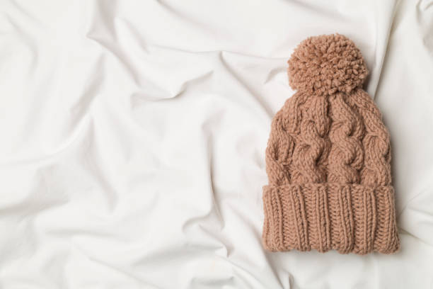 istock Brown winter hat with pompon on white bed sheet. Top view 1458293308