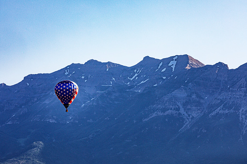 A red, white and blue patriotic USA American flag motif hot air balloon is flying high - drifting over the 