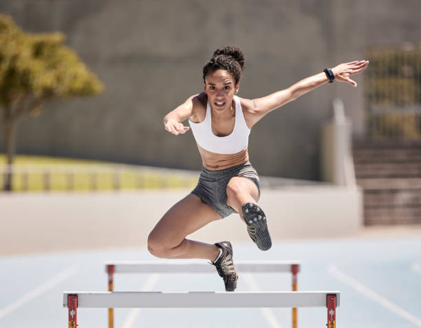 salto, atleta e ostacolare donna nera in gara sportiva, competizione o allenamento allo stadio con energia, potenza e sfida del corpo. veloce, velocità e corridore in un campo da arena o campo per l'esercizio di allenamento - atleta di atletica leggera foto e immagini stock