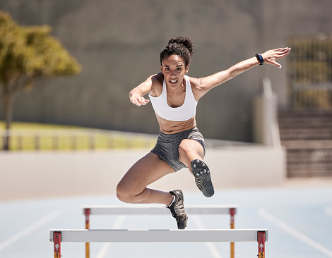 Jump, athlete and hurdle black woman in sports race, competition or training at stadium with energy, power and body challenge. Fast, speed and runner at an arena course or field for workout exercise