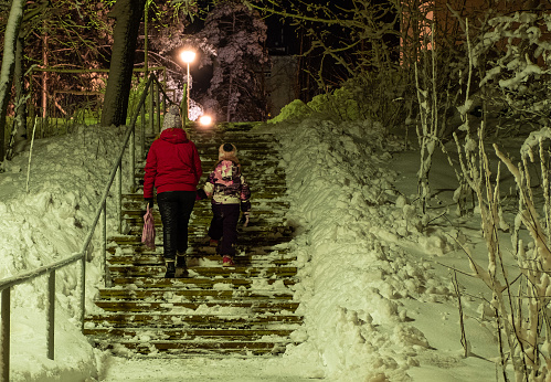City life in Finland Lahti. Young woman, Caucasian, with a child girl 7 years old on the street in winter. The family returns home late in the evening.