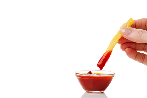 Hand dip french fries chips into ketchup isolated on white background