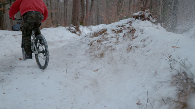 SLOW MOTION: Rear view of mountain biker spraying snow at riding corner on trail
