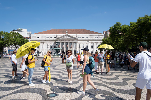 Lisbon, Portugal: a group of tourists looking for a free tour guide with a yellow umbrella, at Rossio Square in Lisbon, Portugal