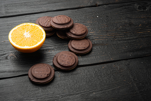 Cakes sweet cookies with orange, chocolate and coffee set, on black wooden table background, with copy space for text