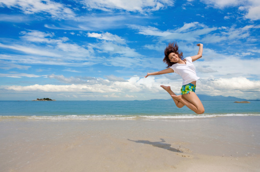 young beautiful girl jumping gracefully on a beautiful day at the beach with beautiful clouds in the background