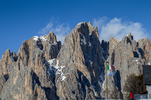 Pra Martin, South Tyrol, Italy - February 14, 2020: typical Dolomites rock formation called Pra Martin in South Tyrol with an Italian flag and the flag of the mountain rescue service on a flagpole in front of it