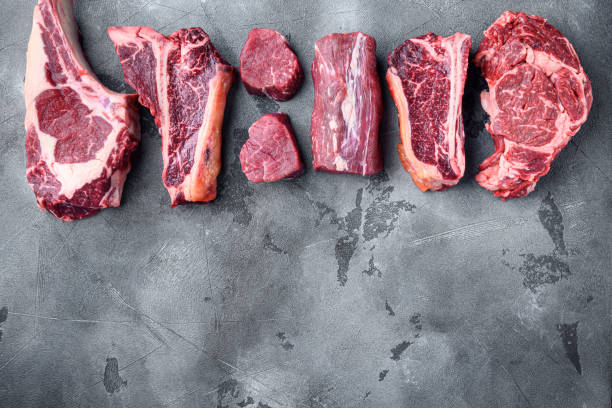 variety of raw beef meat steaks for grilling with seasoning and utensils, tomahawk, t bone, club steak, rib eye and tenderloin cuts, on gray stone background, top view flat lay, with copy space for text - veal t bone steak raw steak imagens e fotografias de stock