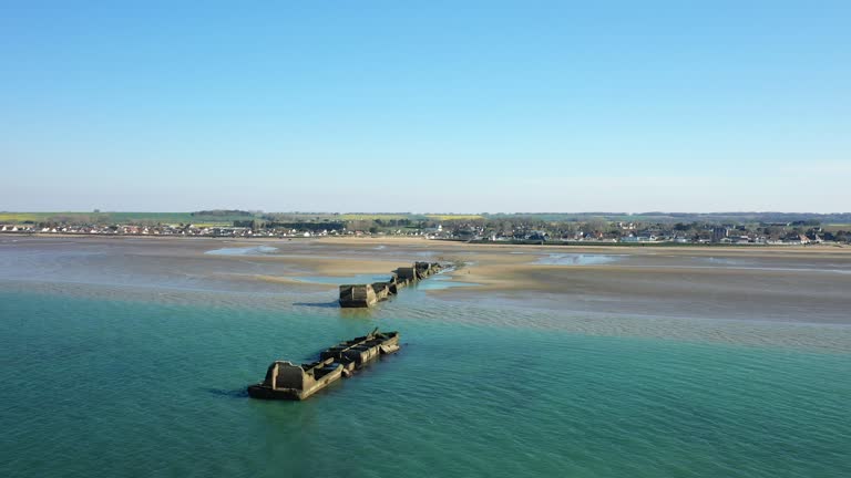 An element of the artificial harbor on the sandy beach of Gold beach in Europe, France, Normandy, towards Arromanches, Asnelles, in spring, on a sunny day.