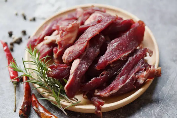 beef jerky with herbs and spices - dried beef on wooden plate, raw dried meat for cooking, dry meat beef in Thailand food