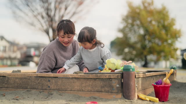 Small girl playing with sand together with her mother in public park