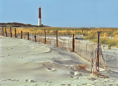 Scenic wide shot of Barnegat Lighthouse with sandy beach and dune grass in foreground
