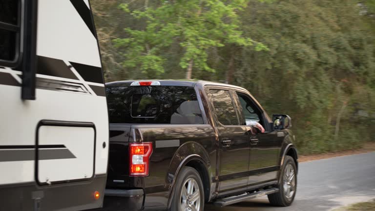 Couple driving camper trailer on rural road, woman waving