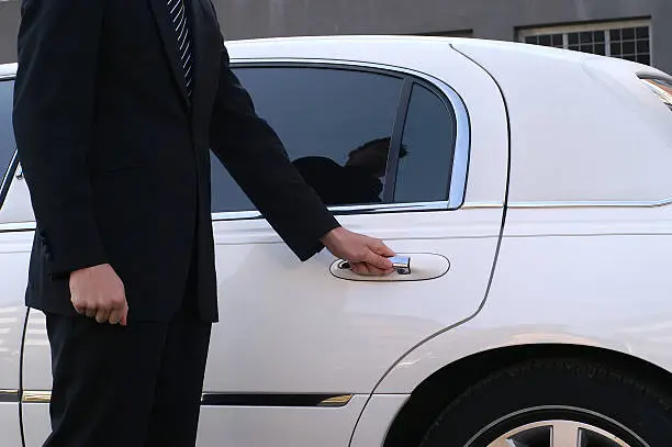 Limousine driver is opening car door for client.