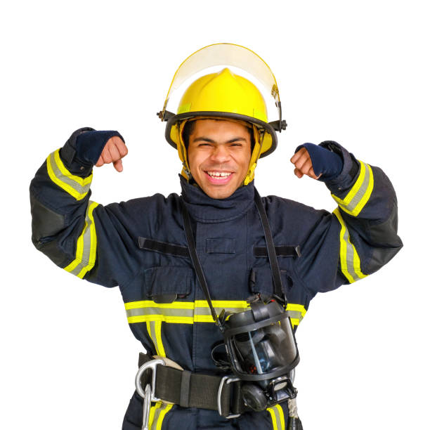 Young smiling African American fireman in fireproof uniform and helmet flexing his biceps, isolated on white background. Fireman showing his muscles.