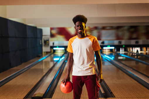 A young black male poses in front of his lane in a bowling alley