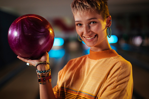 A close-up of a young, attractive female holding a bowling ball in one hand