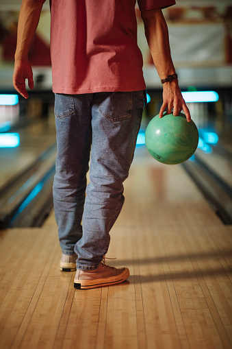 An unrecognizable man standing in front of his lane with a bowling ball