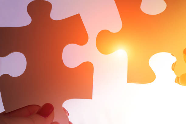 istock two hands trying to connect couple puzzle piece with sunset background. Jigsaw alone puzzle against sun rays. one part of whole. symbol of association and connection. business strategy. 1458344370