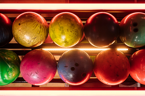 Happy young friends are holding balls, looking at camera and smiling while playing bowling together, girl in the foreground