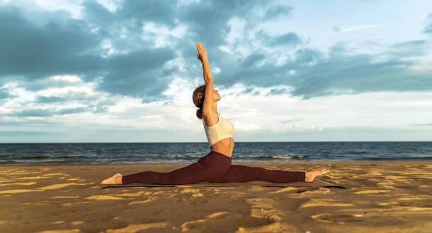 istock Attractive young Caucasian women practicing monkey pose relaxing on the beach. Hanumanasana. 1458344741