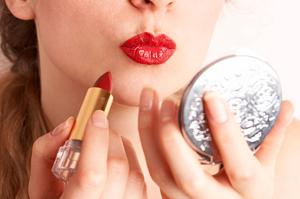 Woman applying red lipstick while looking to hand mirror stock photo