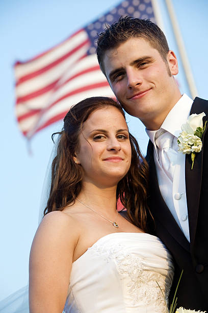 a happy and young attractive couple on their wedding day with an American flag flying in the background