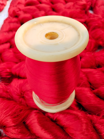 spool and red raw silk extracted from Silk Cocoons that were produced by Silkworms.