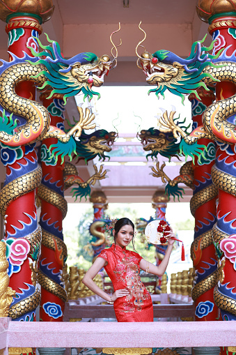 Portrait attractive Asian woman wearing traditional red cheongsam qipao dress in Naja Chinese shrine at Chonburi of Thailand, Chinese new year concept