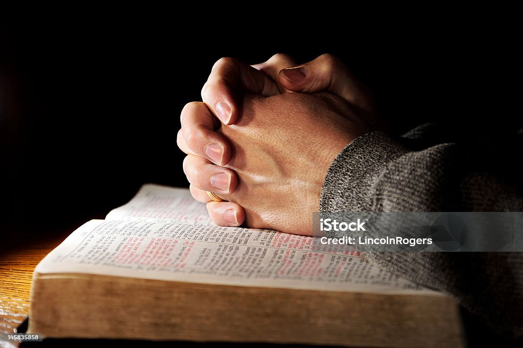 Praying Hands Man & Bible Hands of a man praying in solitude with his Bible (Christian image, shallow focus). Bible Stock Photo