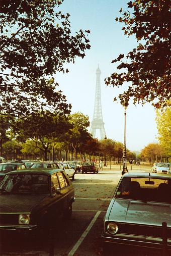 Faded Eiffel Tower in sunlight viewed from treed parking lot with cars\nPhoto adjusted to look vintage, instant film post production. Taken on film, in 1987 and scanned digitally.
