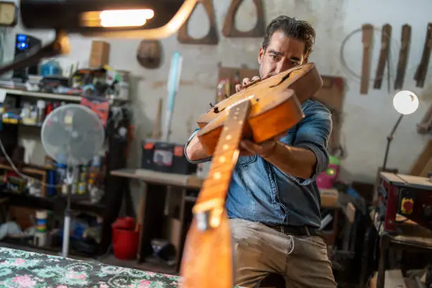 A luthier repairs a vintage semi-acoustic guitar by looking at the neck and fingerboard inside an ancient handcrafted lutherie - small handcraft business and lifestyle people concept