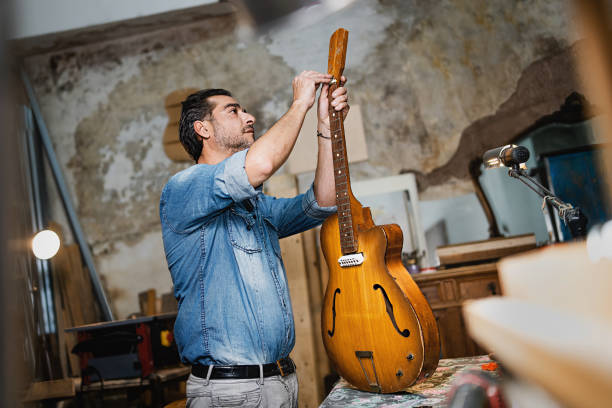 liutaio artigiano che fissa una chitarra avvitando il truss rod - workshop old fashioned old instrument maker foto e immagini stock