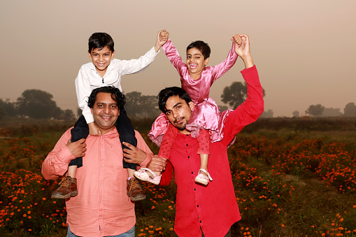 Cheerful Indian family celebrating summer vacation in flower field during springtime portrait with arm raised.