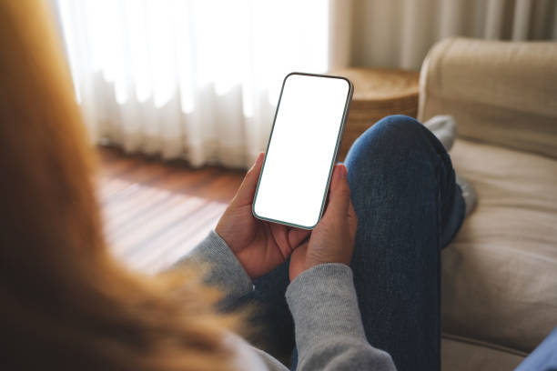 istock Mockup image of a woman holding mobile phone with blank desktop white screen while lying on a sofa at home 1458365840