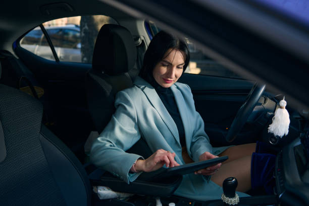 Confident businesswoman on the driver's seat, using digital tablet, telecommuting, planning project. Lifestyle. People stock photo