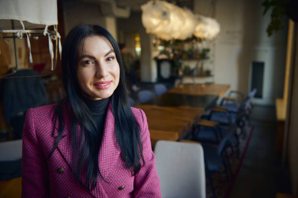 Middle-aged stylish woman, business lady smiling at camera, standing at her workplace in her own cozy modern restaurant stock photo