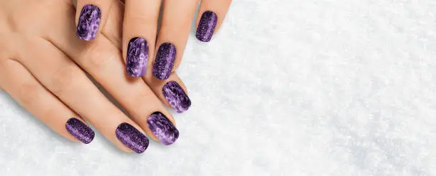 Close-up of a beautiful woman's hands with dark purple glitter nails and soft skin advertises a spa that offers manicures and hand treatments