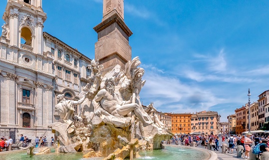 Rome, Italy - June 20, 2014. Ornate statues and Fontana dei Quattro Fiumi in the Piazza Navona in central Rome, surrounded by sightseeing tourists and beautiful baroque architecture.
