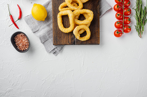 Fried squid rings breaded calamari appetizer set, on serving board, on white stone table background, top view flat lay, with copy space for text