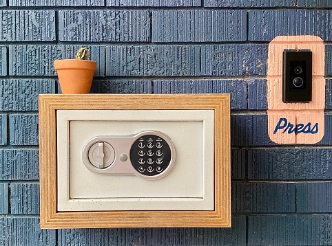 Horizontal safe for room keys with cactus potted plant resting atop, plant on brick wall next to press button at entrance of country hotel door Australia