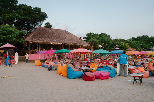 Bali, Indonesia - Circa 2019: Tourists lay on colorful bean bags waiting for sunset at Seminyak beach.