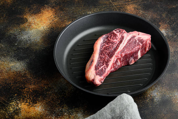 古い暗い素朴な背景に生の新鮮な乾燥熟成牛肉のtボーンステーキ、フライパン - aging process beef old dry ストックフォトと画像