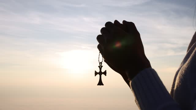 silhouette of Young Woman is Standing and Keeping a Christian Cross in Her Hand at Sunset. the Action in the Real Time. prayer of remembrance of god.